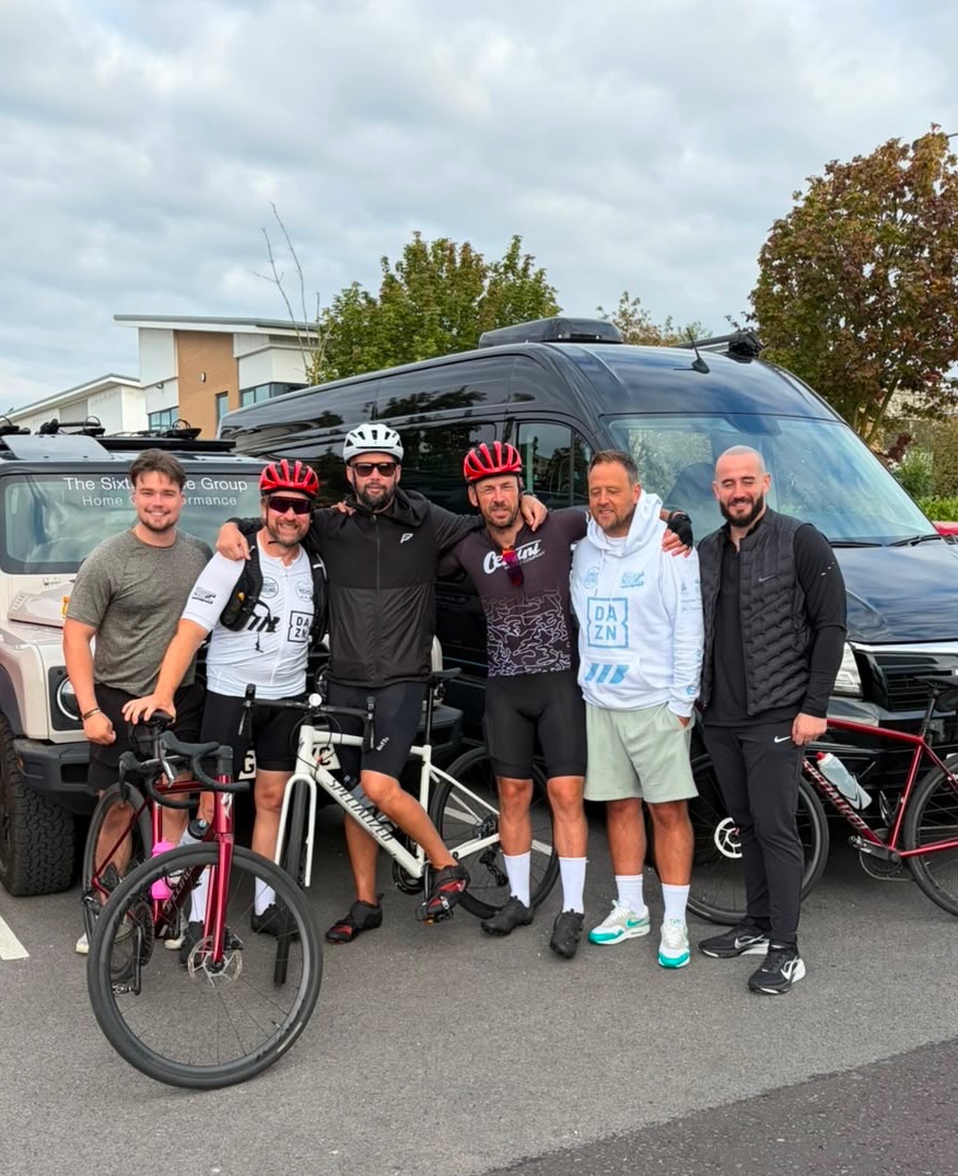 The Longest Round team Mitch Mottram with The Longest Round riders and support crew posing together beside bikes and support vehicles in a car park