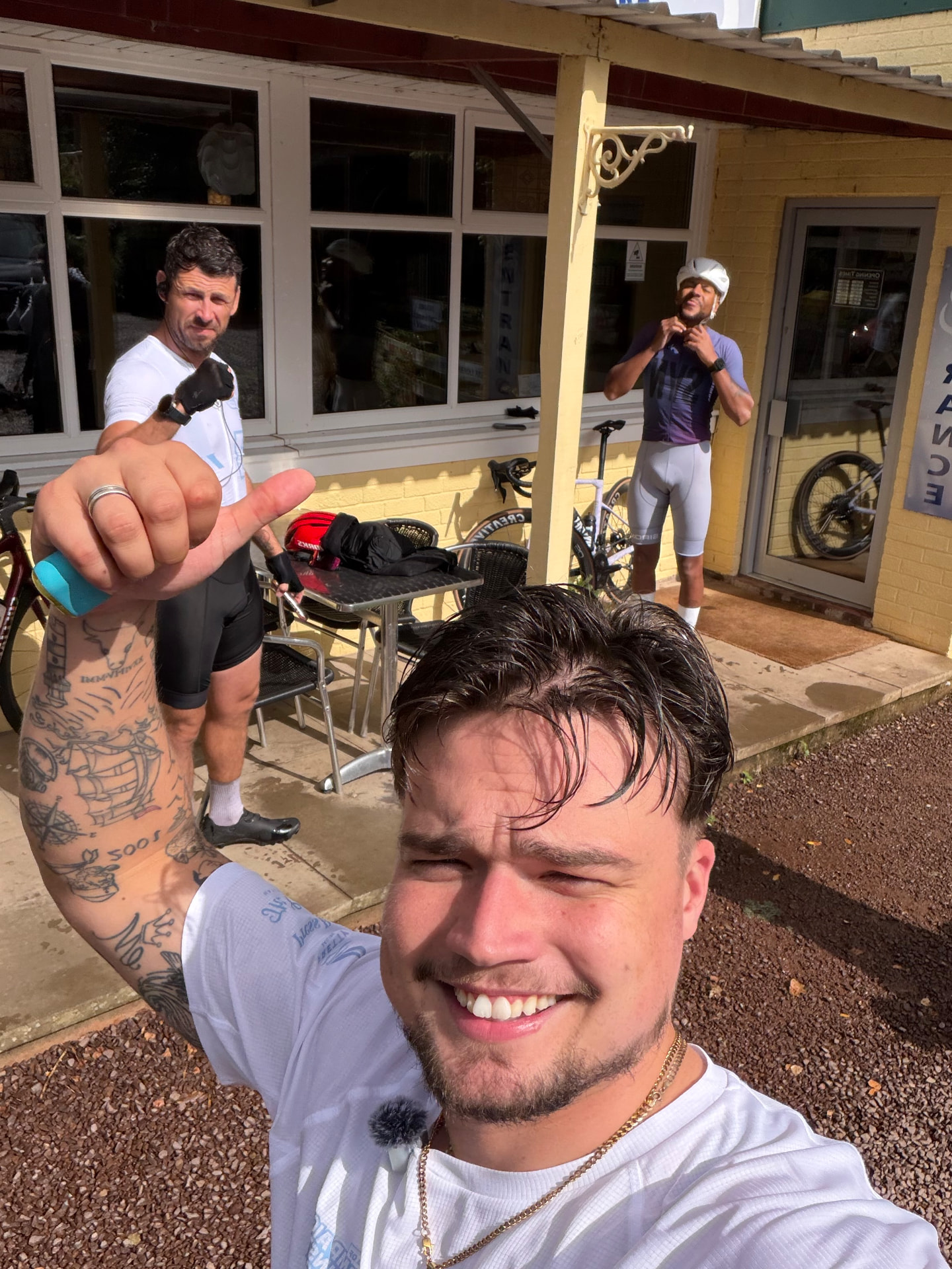 Thumbs up on the roadside Mitch Mottram smiling in a roadside selfie with riders resting outside a cafe part-way through a long day in the saddle