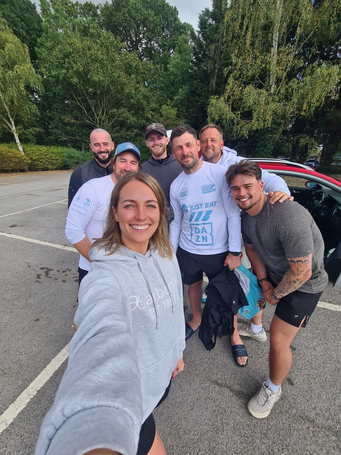 Group selfie of Mitch Mottram with The Longest Round riders and support team in charity jerseys and hoodies before a stage start